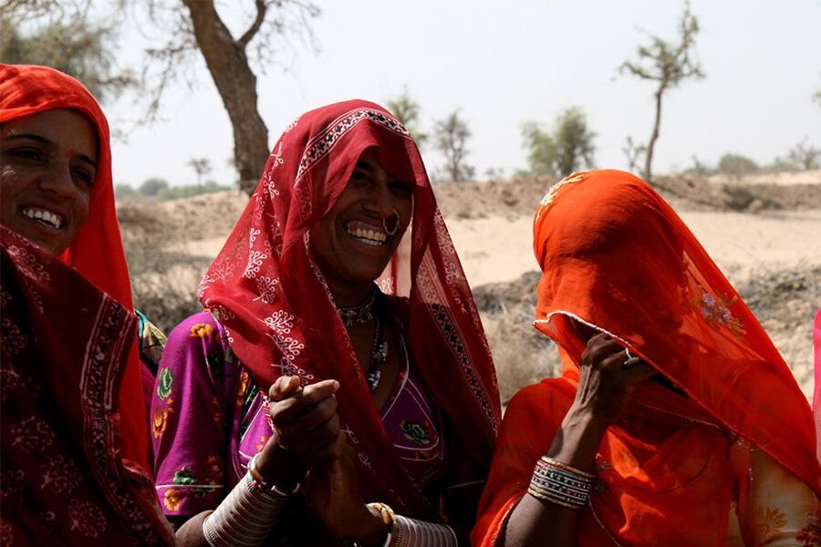 Warm welcomes in the village Smiling Bishnoi women in bright red and orange odhnis, Jodhpur
