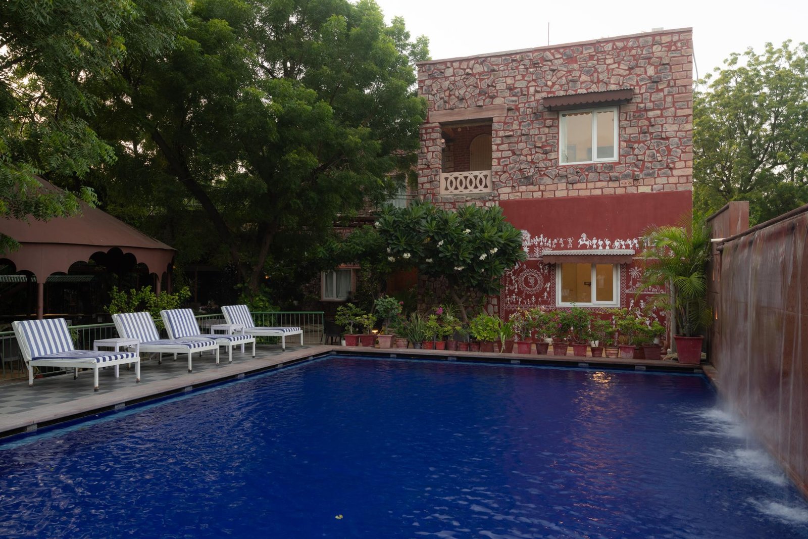 Swimming pool with sun loungers and heritage stone building at The Mandore